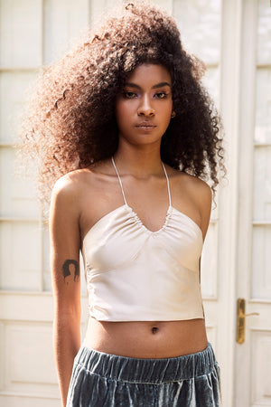 Open image in slideshow, Ruched halter crop top featuring an ivory satin fabric and an open tie back. Team it with some cute pants!
